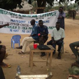Local people sit around a banner that asks people not to hunt or eat pangolins.